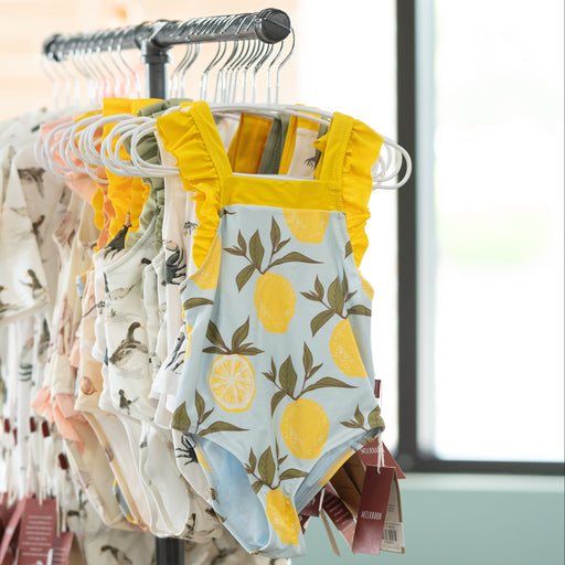 Baby clothes on hangers with colorful designs in a room with large windows.