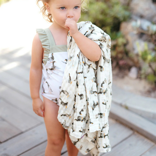 Child wrapped in a white blanket with mallard duck  patterns on a wooden deck.