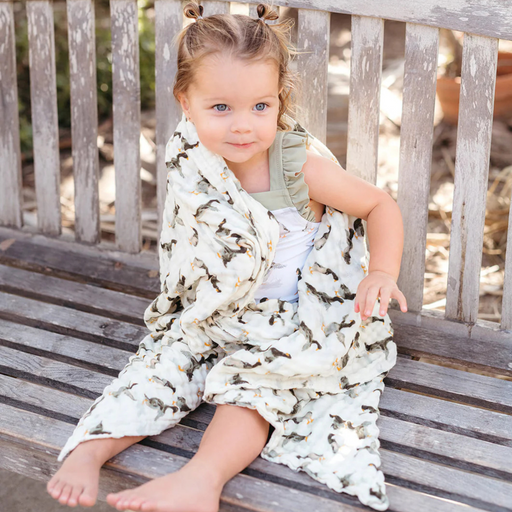 Child sitting on a wooden bench with a mallard duck patterned blanket draped over them