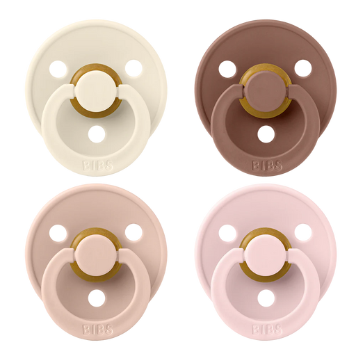 Four BIBS round pacifiers shown together, featuring cream, brown, blush pink, and soft pink shields with ventilation holes