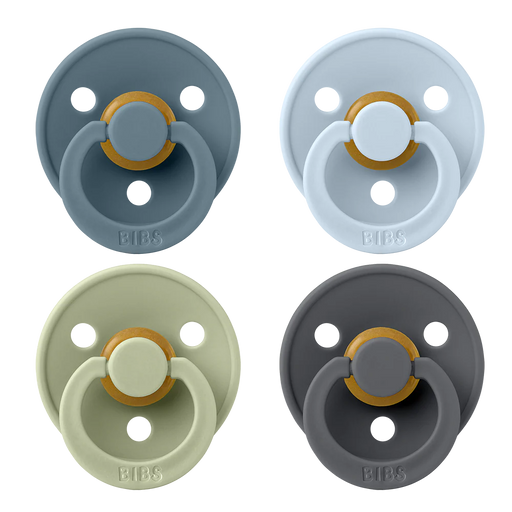 Four BIBS round pacifiers shown together, featuring blue, light blue, sage green, and dark gray shields with ventilation holes