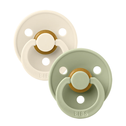 Two BIBS round pacifiers shown together, featuring an ivory pacifier and a sage green pacifier with round shields