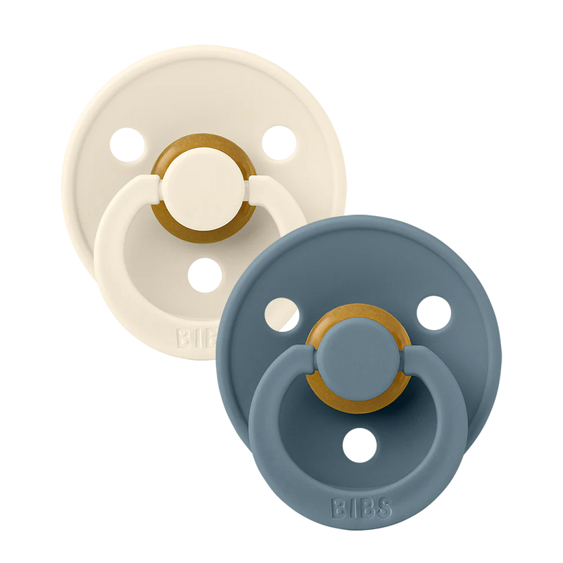 Two BIBS round pacifiers shown together, featuring a cream-colored pacifier and a blue-toned pacifier with round shields