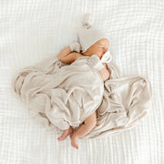 Sleeping newborn in a knotted hat wrapped in the Lou Lou & Co Dakota cream plush knit swaddle