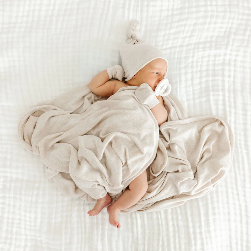 Sleeping newborn in a knotted hat wrapped in the Lou Lou & Co Dakota cream plush knit swaddle