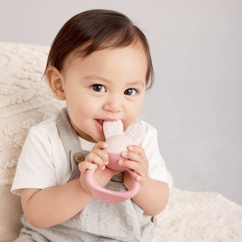 Baby holding a pink teething ring against a neutral background