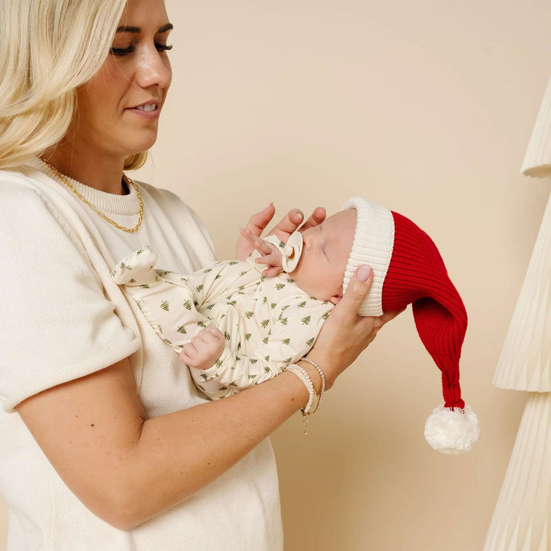 Mom holding newborn in Lou Lou & Co Kevin Christmas tree zipper footie and red Santa hat