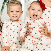 Two smiling siblings wearing matching Lou Lou & Co Santa Baby zipper footies