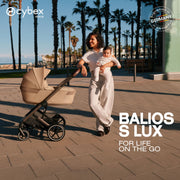 Mom and baby walking with Cybex Balios S Lux stroller and Fold Cot by palm trees
