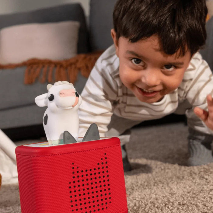 Child playing with toy cow and red tonies box on the floor
