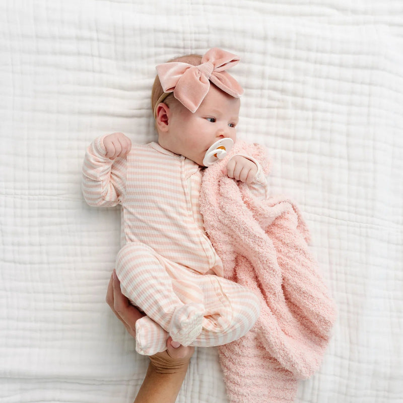Newborn in the Lou Lou & Co Harper pink striped footie and pink bow, cuddling a pink knit blanket