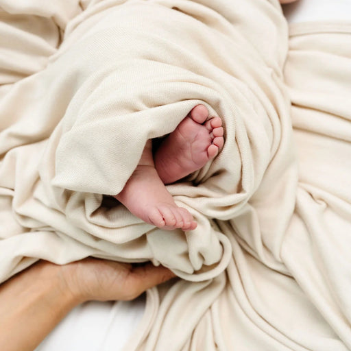 Baby's feet peeking out from the Lou Lou & Co Dakota cream plush knit swaddle blanket