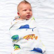 Baby wrapped in a colorful fish-patterned swaddle on a white blanket