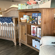 Wooden bookcase filled with baby items and a crib in the background