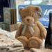 Teddy bear with a tag, folded baby clothes, and books on a table.