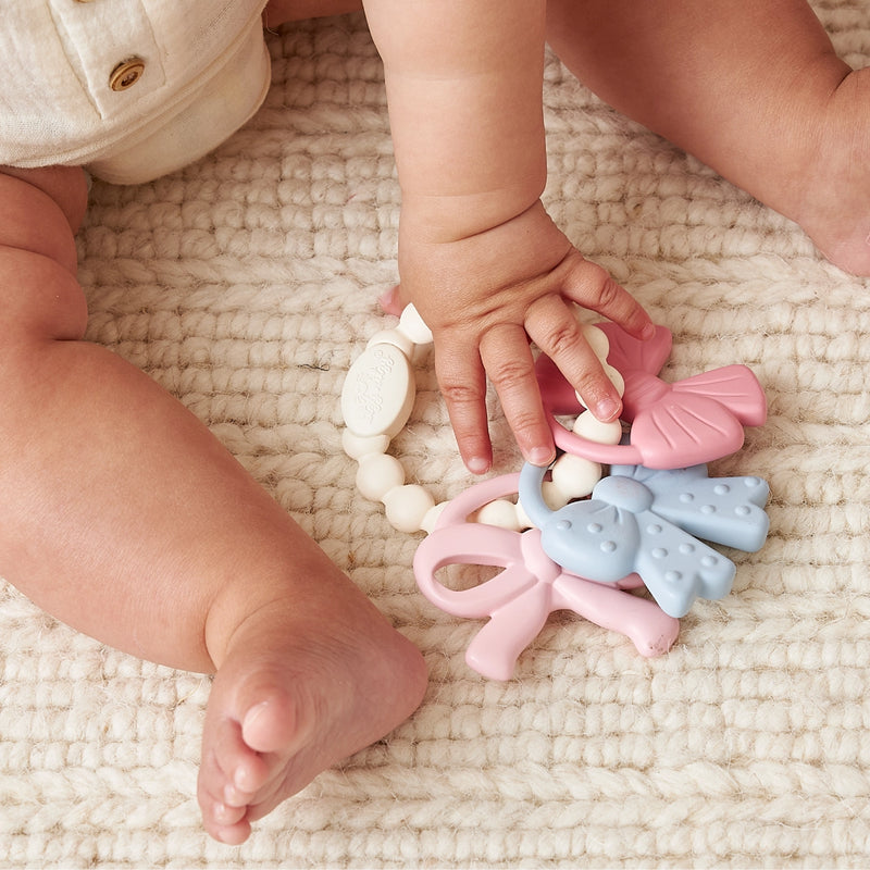 Baby sitting on a mat holding and exploring the silicone teething ring