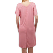 A woman viewed from the back wearing a short-sleeve pink nightshirt or sleep dress, standing against a plain white background.