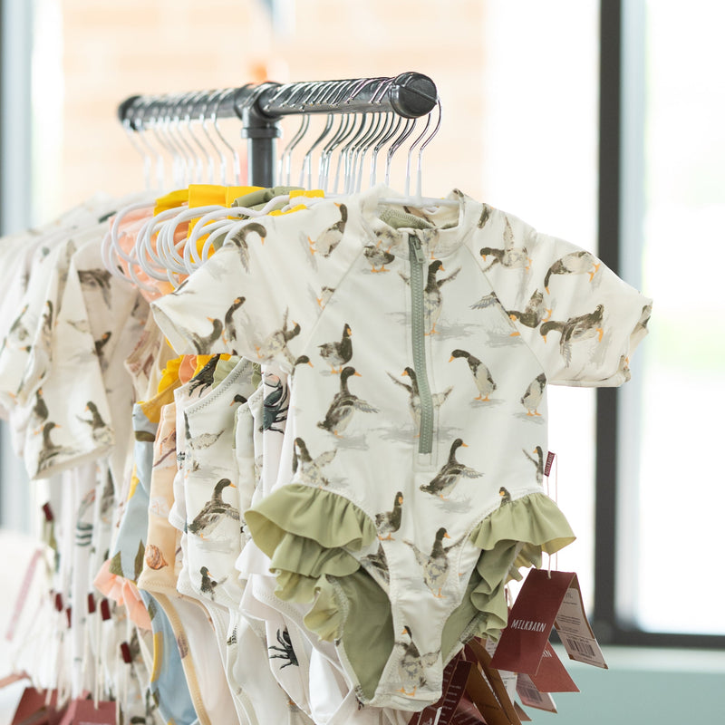 Clothing rack with patterned baby toddle swimwear in a room with large windows