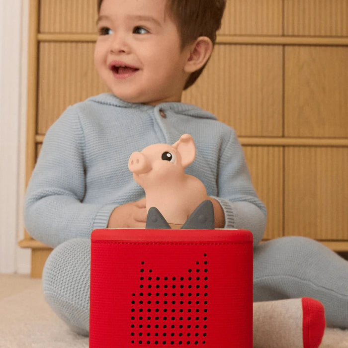 Child holding a pink pig on a red tonies box