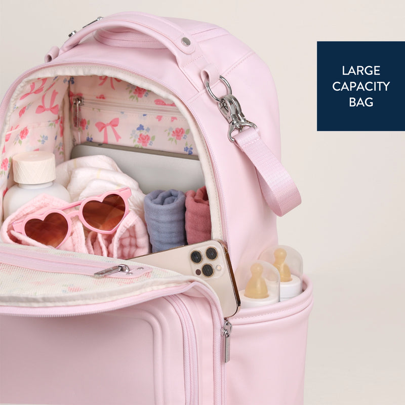 Open backpack diaper bag filled with baby essentials including bottles, shoes, and accessories