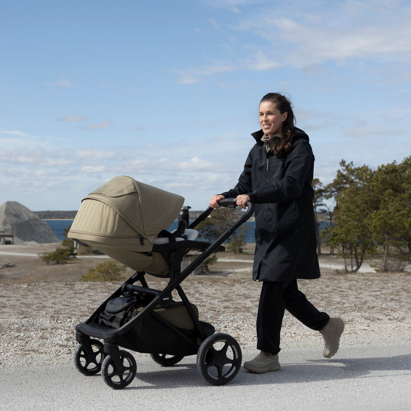 Mom pushing Thule Charm stroller with bassinet along a coastal path