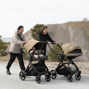Two parents pushing Thule Charm strollers on a gravel path