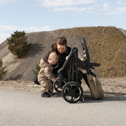 Parent hugging toddler next to folded Thule Charm stroller
