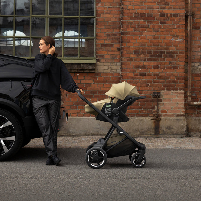 Parent with Thule Charm stroller and car seat by a brick building