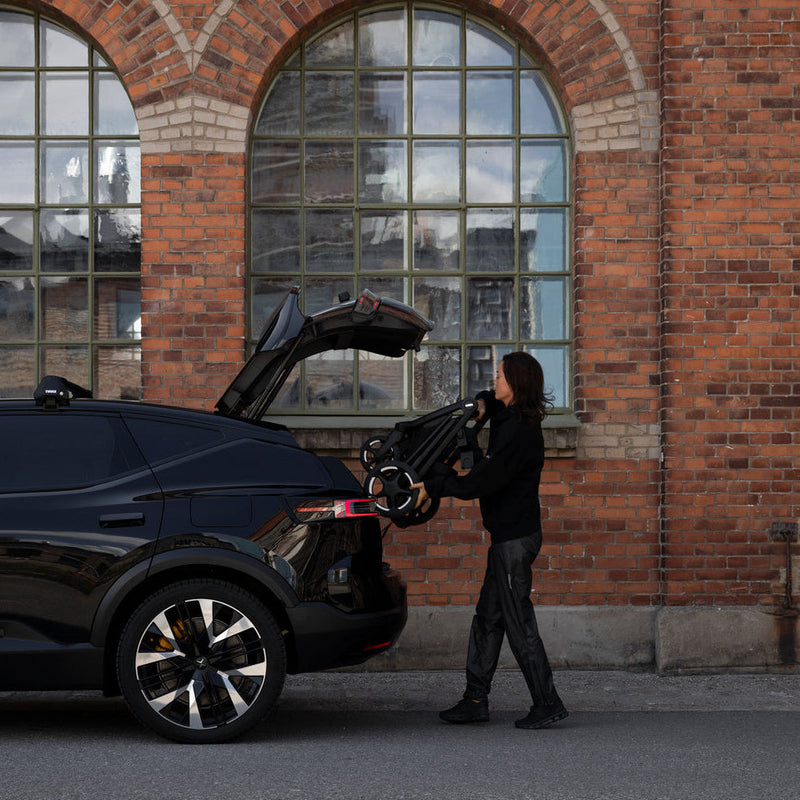 Parent loading Thule Charm stroller into a car trunk