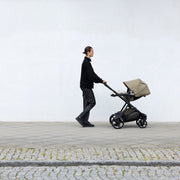Parent walking with Thule Charm stroller along a white wall