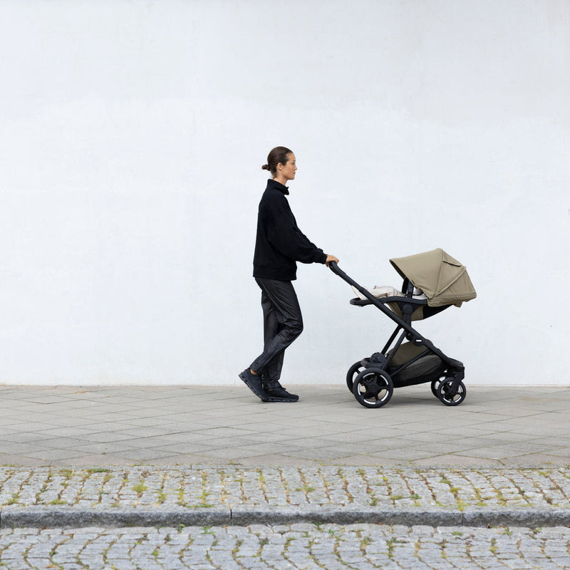 Parent walking with Thule Charm stroller along a white wall