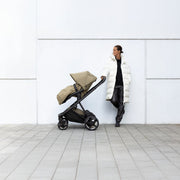 Parent standing beside Thule Charm stroller with footmuff against a white wall