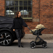 Parent with Thule Charm stroller and Thule Maple car seat beside a car