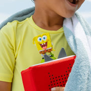 Child wearing a yellow shirt with a cartoon character, holding a red object, with a towel draped over their shoulders.