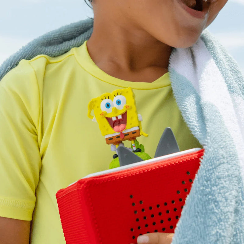 Child wearing a yellow shirt with a cartoon character, holding a red object, with a towel draped over their shoulders.