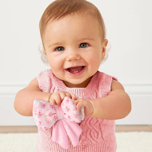 Baby holding the Sweetie Crinkle toy while wearing it on their wrist