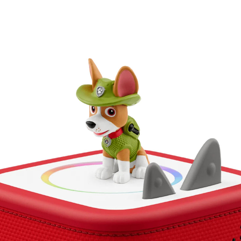 A Paw Patrol toy figurine of Chase standing on top of a red, cube-shaped speaker or device with a white top panel, set against a plain white background.