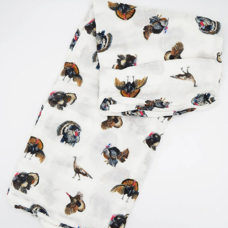 A white muslin baby blanket or scarf featuring an all-over print of painted wild turkeys in brown, black, and orange, folded neatly on a white background.