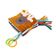 A plush, ribbed brown soft baby book with a cute moose face on the cover, colorful fabric tags on the side, and two attached teething rings (one green beaded, one orange smooth).