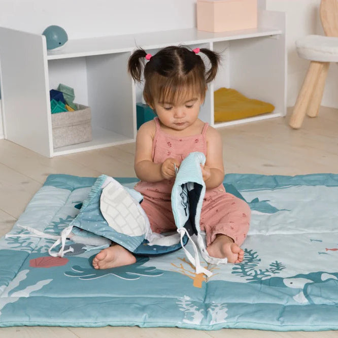 Child interacting with the open soft book on a play mat.