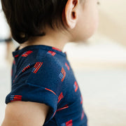 Child wearing a navy blue shirt with red and white pattern, standing indoors.