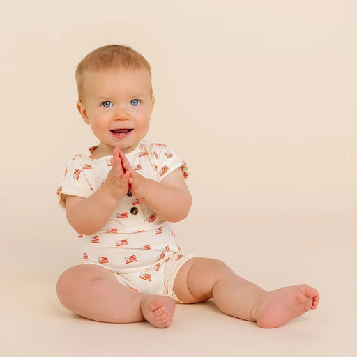 Baby sitting on a beige surface wearing an american flag romper