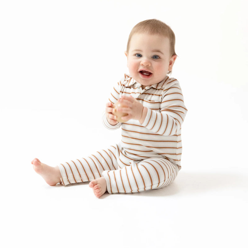 Baby wearing brown vintage-stripe polo romper, sitting and smiling.