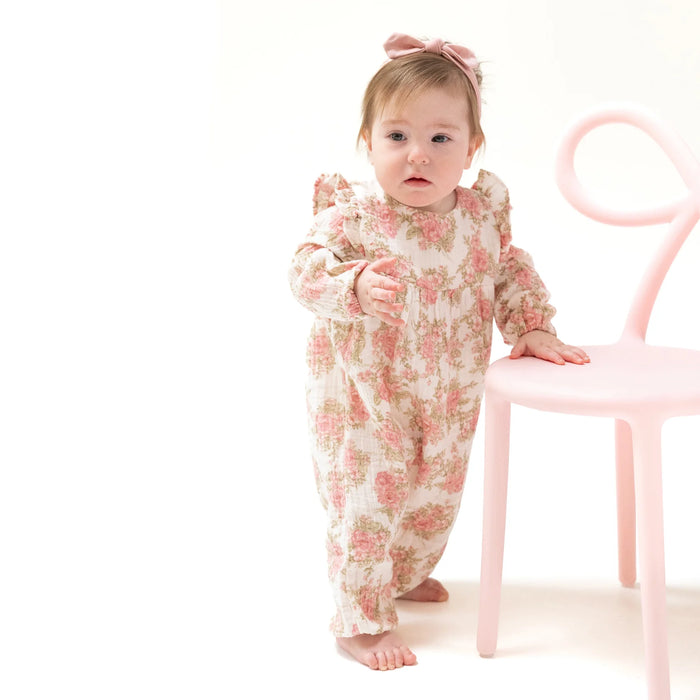 Toddler wearing the Heirloom Bouquets ruffle sleeve romper, standing by a chair
