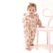 Toddler wearing the Heirloom Bouquets ruffle sleeve romper, standing by a chair