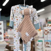 A baby sleepwear set displayed on a hanger in a retail store, featuring a white long-sleeve footed onesie with a sports ball pattern and light blue cuffs and collar, paired with a plush tan security blanket.