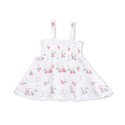 A white sleeveless baby dress with thin shoulder straps, featuring an allover print of pink and blue golf carts and golf clubs on a clean white background.