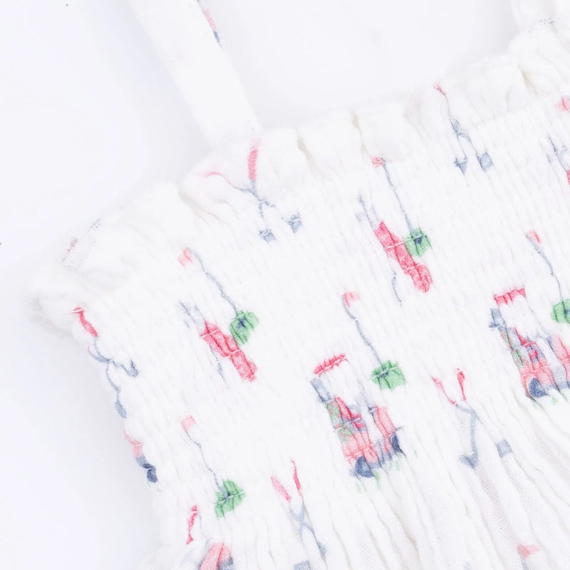 White smocked fabric garment with a delicate multicolor pattern of pink, green, and blue embroidered details, shown in a close-up view.
