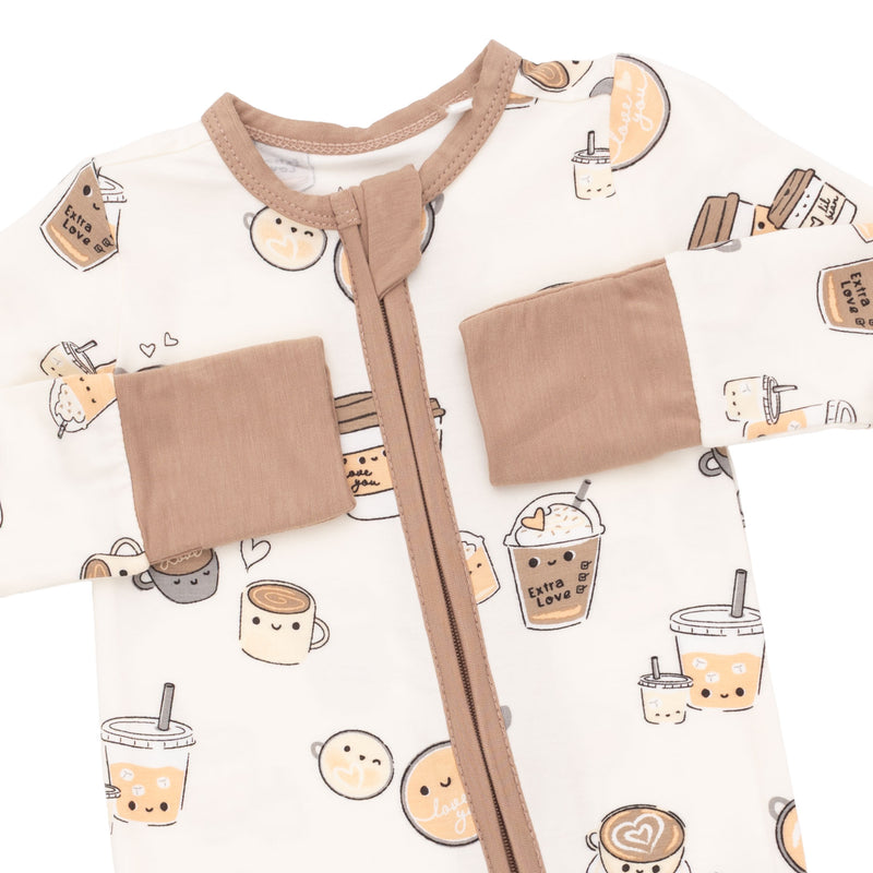 A close-up of a baby sleep sack or romper featuring a cute cartoon bubble tea and coffee cup pattern on an off-white background, with tan trim, a front zipper, and two patch pockets.