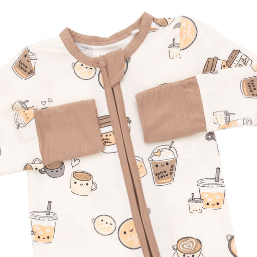 A close-up of a baby sleep sack or romper featuring a cute cartoon bubble tea and coffee cup pattern on an off-white background, with tan trim, a front zipper, and two patch pockets.
